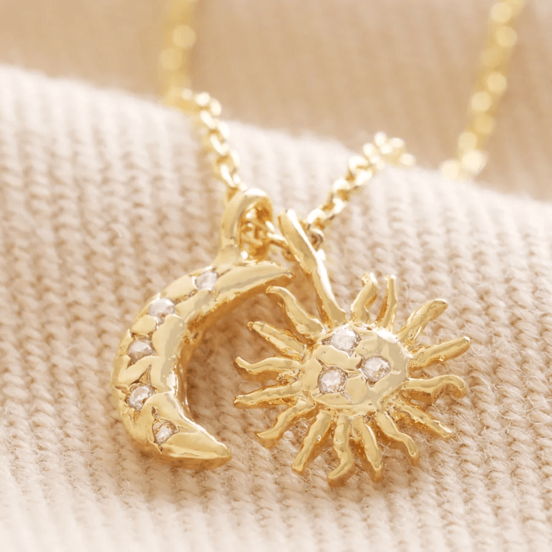 Close-up of gold plated sunburst and crescent moon charms with cubic zirconia crystals on a delicate chain.