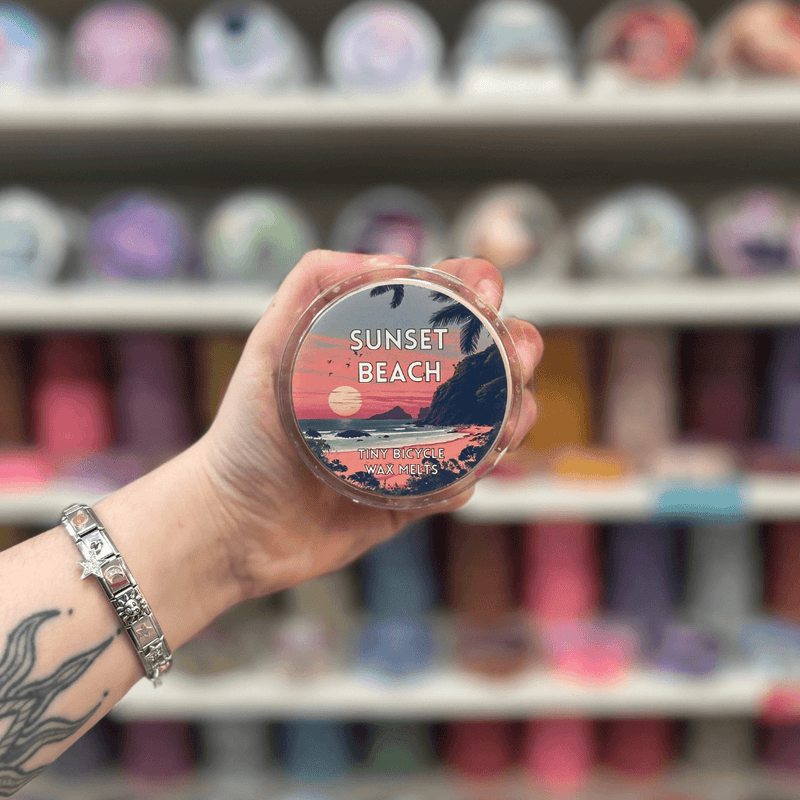 Sunset Beach wax melt pot held in hand with colourful wax melt display in the background