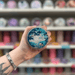 Sweet Nothings wax melt pot held in hand with colourful wax melt display in the background