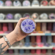 Sweetpea wax melt pot held in hand with colourful wax melt display in the background