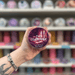 The Comforter wax melt pot held in hand with colourful wax melt display in the background