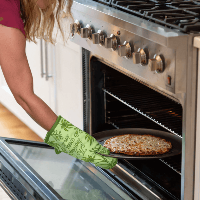 Green novelty oven mitt used to remove a hot pan from the oven.

