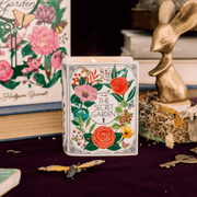 The Secret Garden book candle lit on a styled display with keys, butterfly décor and books behind.