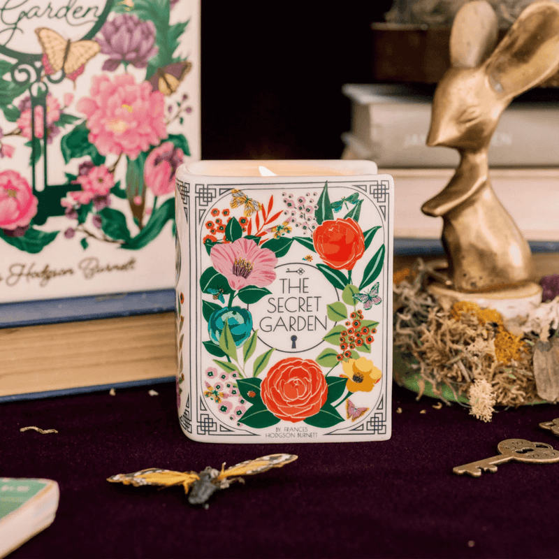 The Secret Garden book candle lit on a styled display with keys, butterfly décor and books behind.