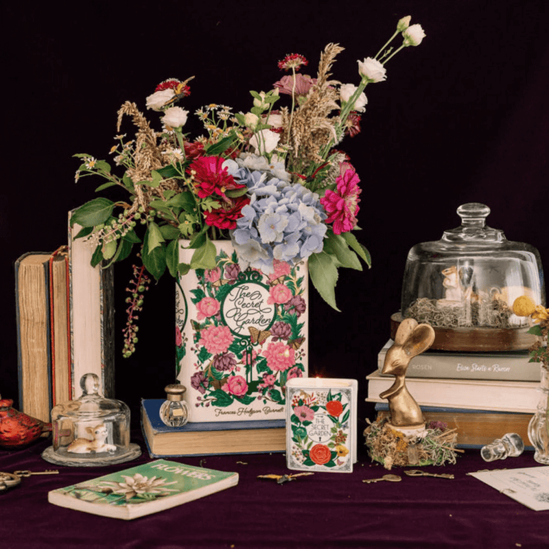 Wide styled scene featuring The Secret Garden book shaped candle with floral book vase and decorative accessories.