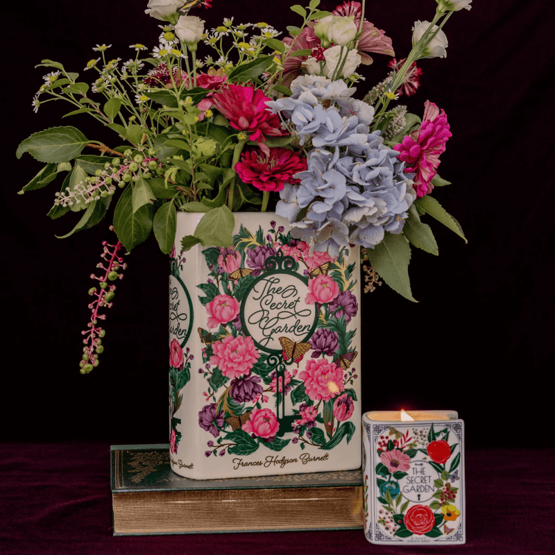The Secret Garden book shaped ceramic vase with colourful floral design, styled with a large bouquet and a matching candle.
