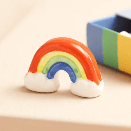 Glazed ceramic rainbow token displayed outside the colourful matchbox packaging