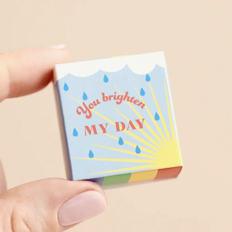 Hand holding the tiny matchbox rainbow token with you brighten my day message on the lid