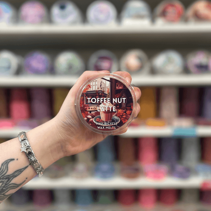 Toffee Nut Latte wax melt pot held in hand with colourful wax melt display in the background