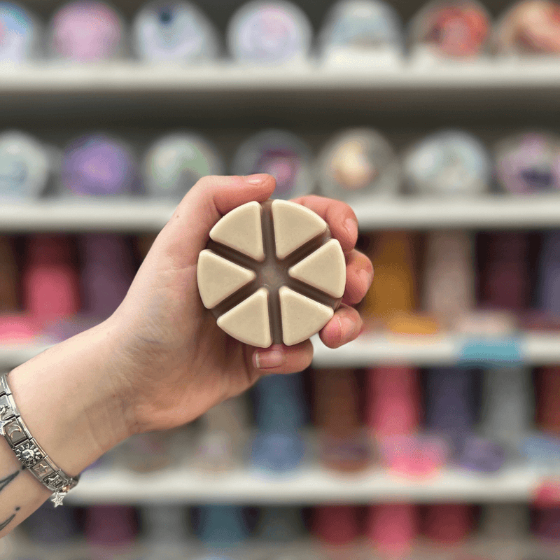 Toffee Nut Latte wax melt segments held in hand with colourful wax melt display in the background