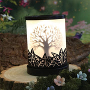 Tree of Life electric wax melt burner lit in a styled woodland setting on a wooden slice with moss and flowers.