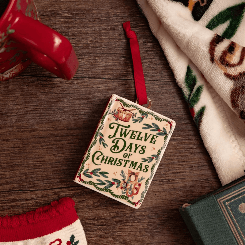 Twelve Days of Christmas ceramic book ornament displayed on a wooden table beside festive accessories