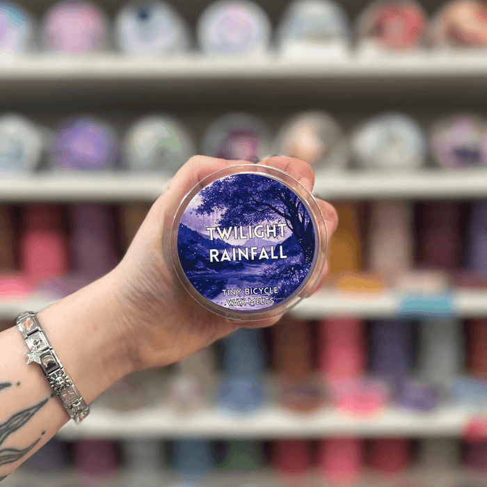Twilight Rainfall wax melt pot held in hand with colourful wax melt display in the background