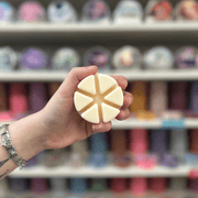 Cream segmented wax melt held in hand in front of a colourful wax melt shelf