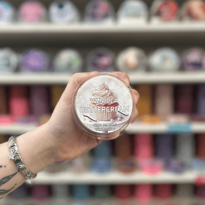 Vanilla Buttercream wax melt pot held in hand with a colourful wax melt display behind