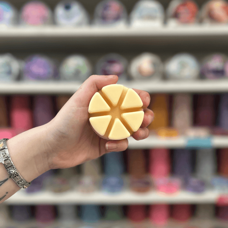 Pale yellow segmented wax melt held in hand in front of a colourful wax melt display