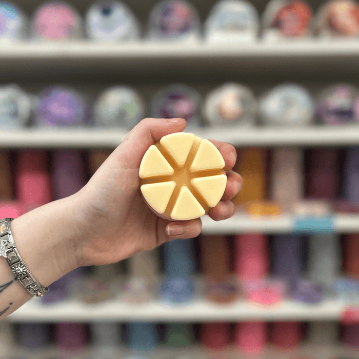 Pale yellow segmented wax melt held in hand in front of a colourful wax melt display