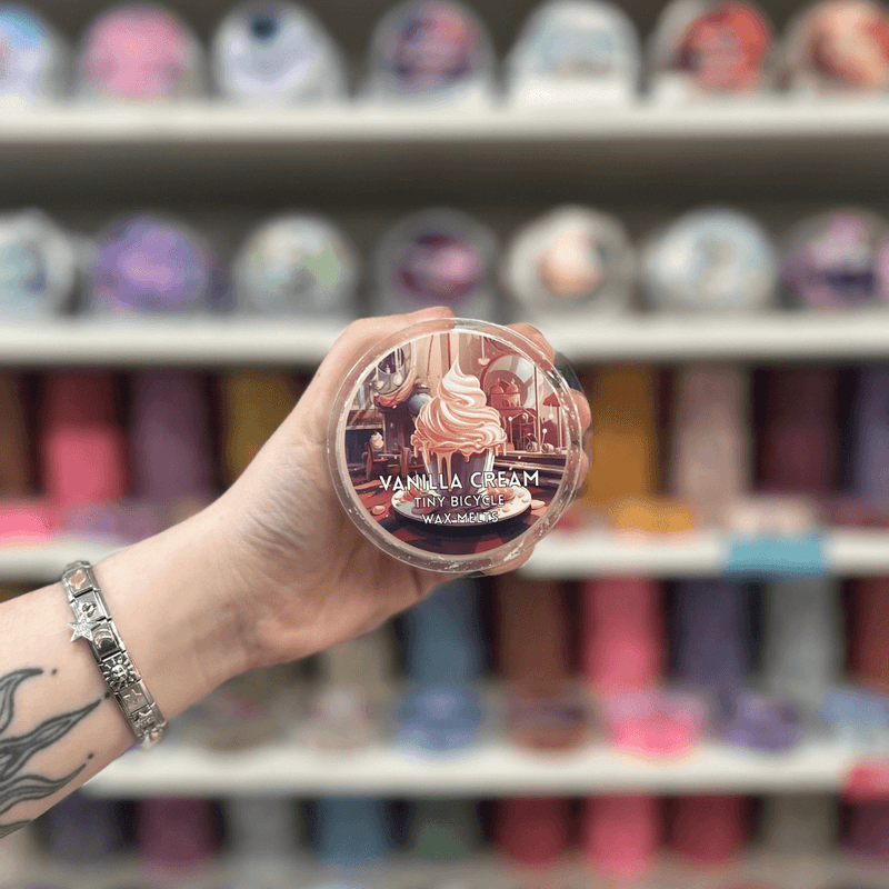 Vanilla Cream wax melt pot held in hand with colourful wax melts blurred in the background