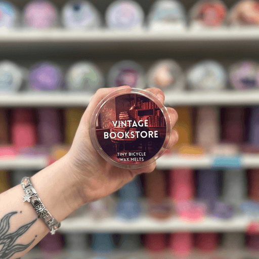 Vintage Bookstore wax melt pot held in hand with colourful wax melt display in the background