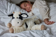 Child sleeping beside Warmies Laying Cow plush toy in bed