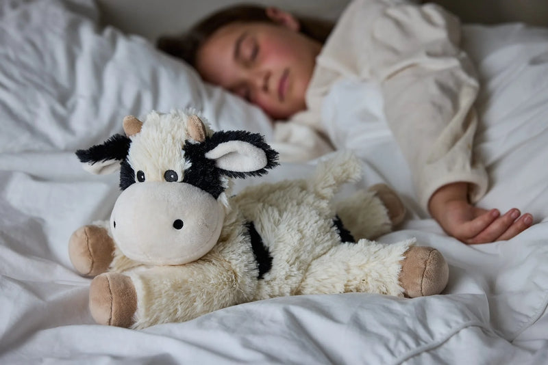 Child sleeping beside Warmies Laying Cow plush toy in bed