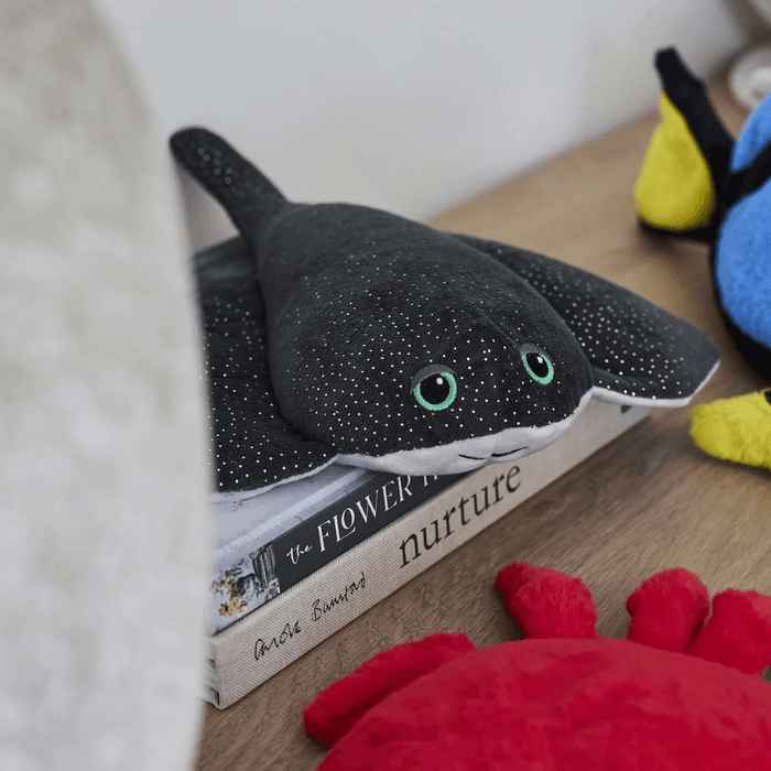 Warmies Manta Ray plush toy displayed on books