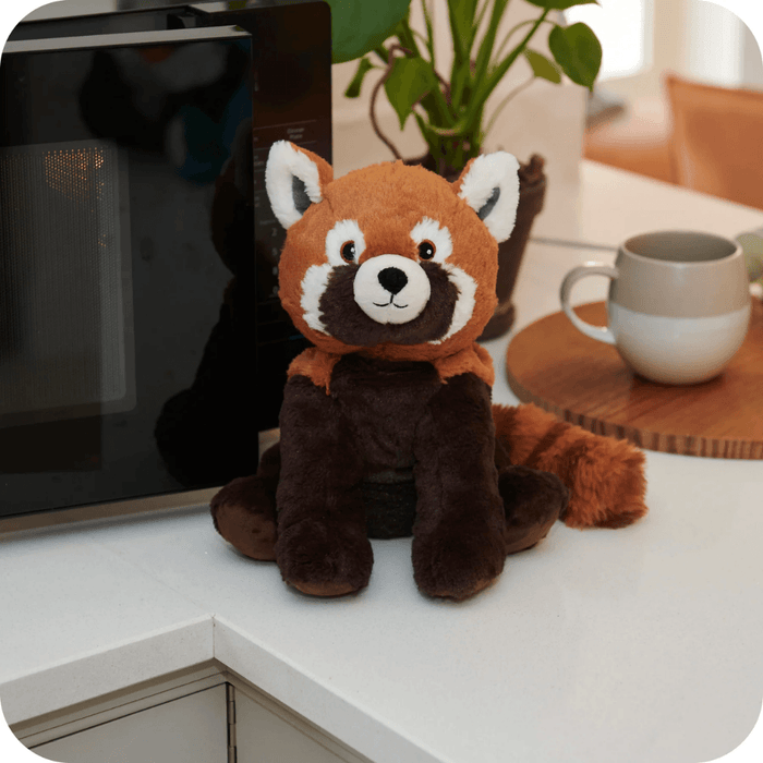 Warmies Red Panda plush toy beside a microwave on a kitchen counter