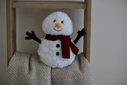 Warmies Snowman plush on a blanket ladder in a cosy home setting.