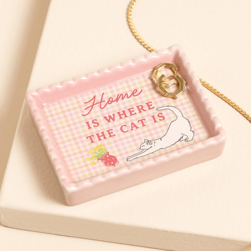 Close-up of pink scalloped ceramic trinket dish with stretching cat and Home Is Where The Cat Is text, holding gold rings.