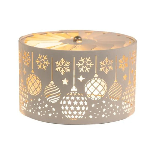 White and gold carousel candle shade with Christmas baubles, snowflakes, and stars, glowing above a candle.

