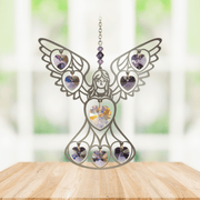 Handmade purple-crystal angel suncatcher displayed on a wooden table in front of a bright window

