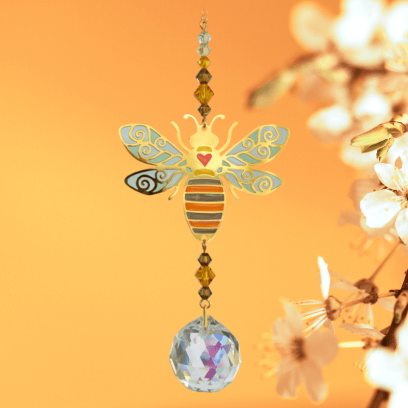 Bee Autumn Gold crystal suncatcher glinting beside blossom against a warm orange sky

