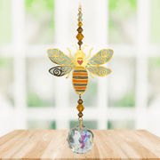 Handmade Bee Autumn Gold crystal suncatcher displayed on a wooden table before a bright window

