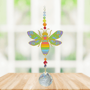 Handmade Bee Rainbow crystal suncatcher displayed on a wooden table in front of a bright window

