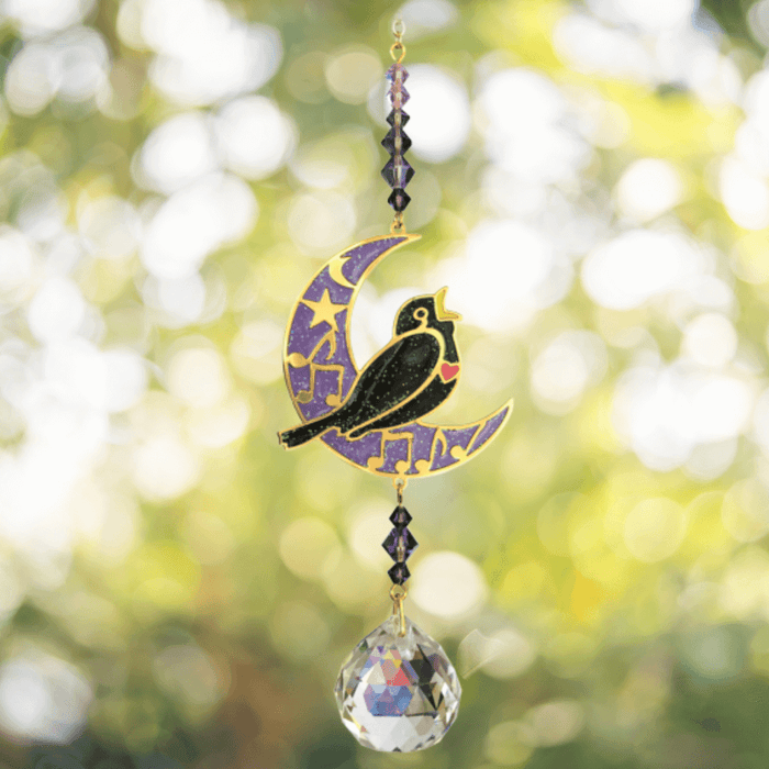 Blackbird Moonlight Crystal Suncatcher hanging in garden sunlight – blackbird on purple crescent moon with amethyst beads and 20 mm crystal ball rainbowing the air.
