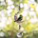 Blackbird Moonlight Crystal Suncatcher hanging in garden sunlight – blackbird on purple crescent moon with amethyst beads and 20 mm crystal ball rainbowing the air.
