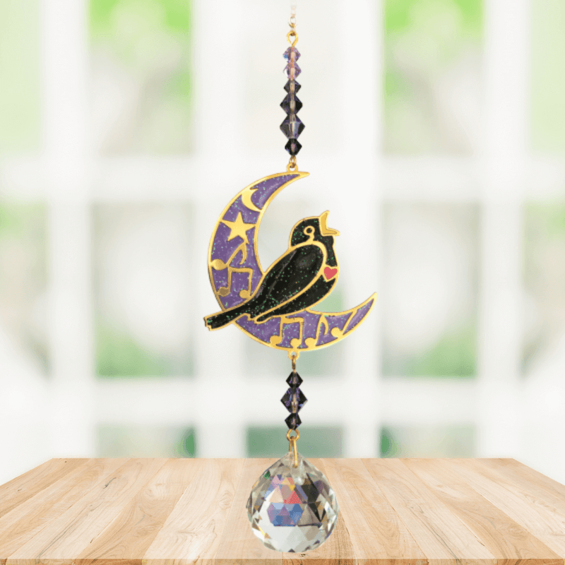 Blackbird Moonlight Crystal Suncatcher displayed by a bright window; crescent-moon motif, dark bird silhouette and crystal ball ready to cast rainbow shards indoors.


