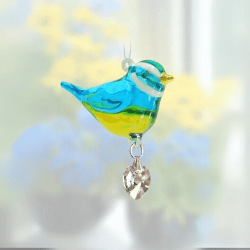 Handmade blue-and-yellow Blue Tit crystal suncatcher sparkling before soft flowers

