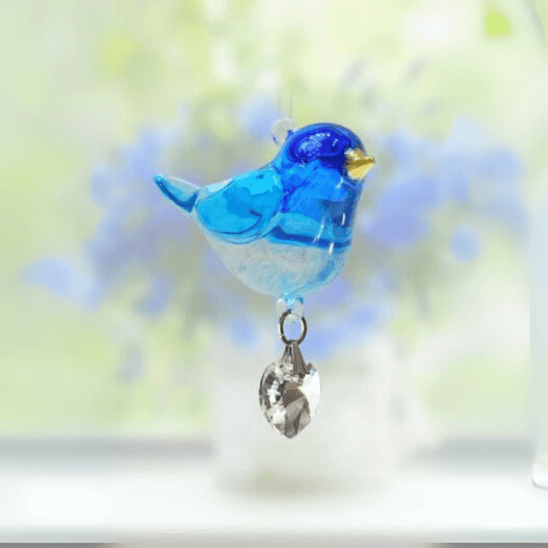 Blue glass Bluebird crystal suncatcher catching sunlight before a soft floral blur

