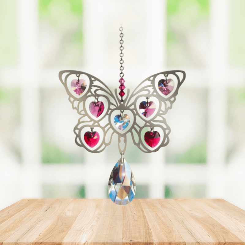 Handmade Butterfly Fuchsia crystal suncatcher displayed on a wooden table in front of a sunny window

