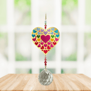 Wild Things Crystal Wonders Heart of Hearts crystal suncatcher hanging in a bright window, mirror-gold heart motif with colourful hearts and 30mm crystal ball.