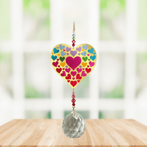 Wild Things Crystal Wonders Heart of Hearts crystal suncatcher hanging in a bright window, mirror-gold heart motif with colourful hearts and 30mm crystal ball.