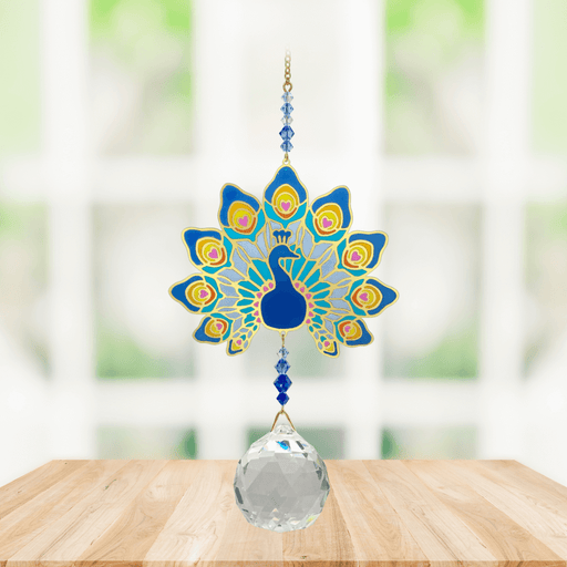 Wild Things Crystal Wonders majestic peacock crystal suncatcher hanging in a bright window, mirror-gold peacock motif in blue with 30mm crystal ball pendant.