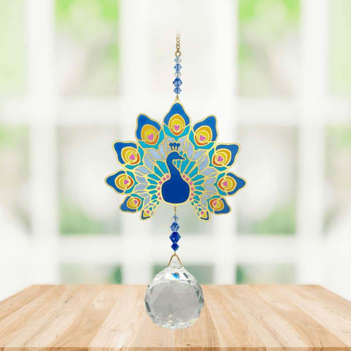 Wild Things Crystal Wonders majestic peacock crystal suncatcher hanging in a bright window, mirror-gold peacock motif in blue with 30mm crystal ball pendant.