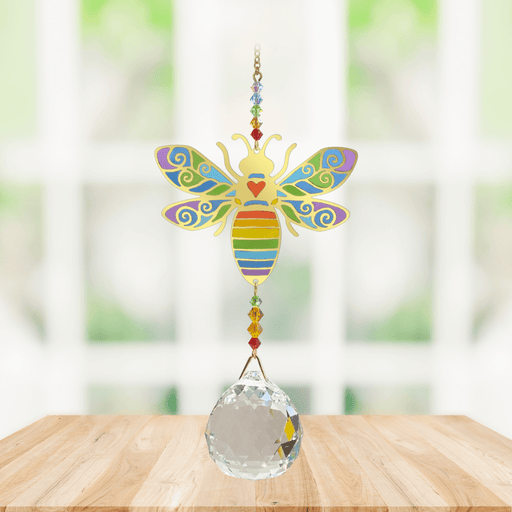 Wild Things Crystal Wonders rainbow bee crystal suncatcher hanging in a bright window, mirror-gold bee motif with rainbow detail and crystal ball pendant.