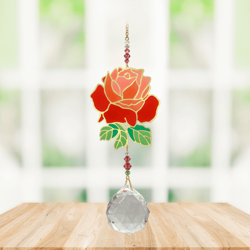 Wild Things Crystal Wonders rose crystal suncatcher hanging in a bright window, mirror-gold rose motif with red petals and 30mm crystal ball pendant.