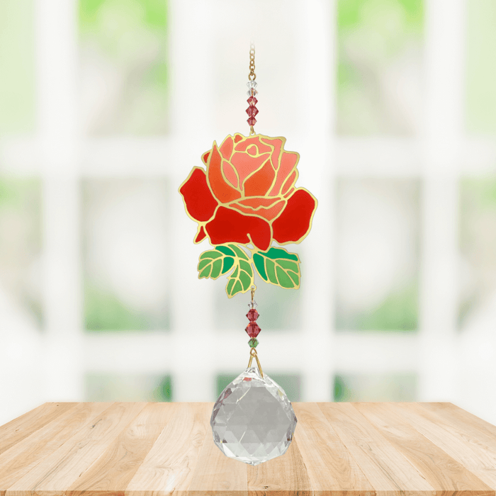 Wild Things Crystal Wonders rose crystal suncatcher hanging in a bright window, mirror-gold rose motif with red petals and 30mm crystal ball pendant.