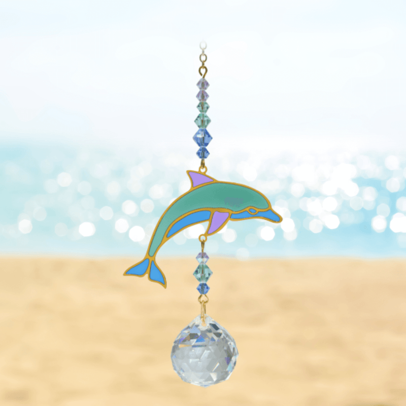 Dolphin Marine Crystal Suncatcher against a bright beach scene – turquoise dolphin, ocean-tone bead cascade and 20 mm prism casting rainbows.

