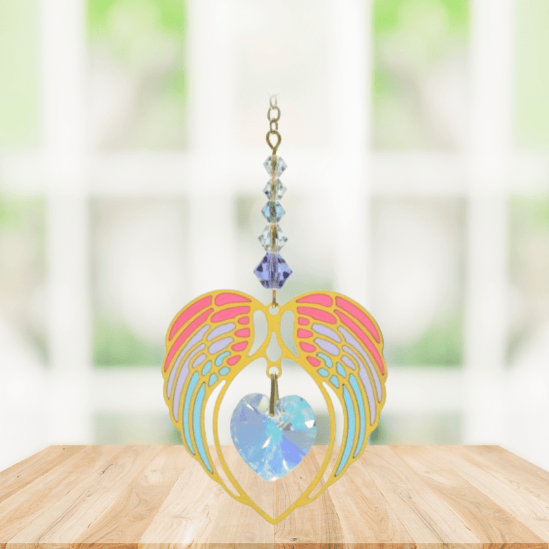 Gold angel wing heart suncatcher with aurora borealis crystal hanging in a bright window
