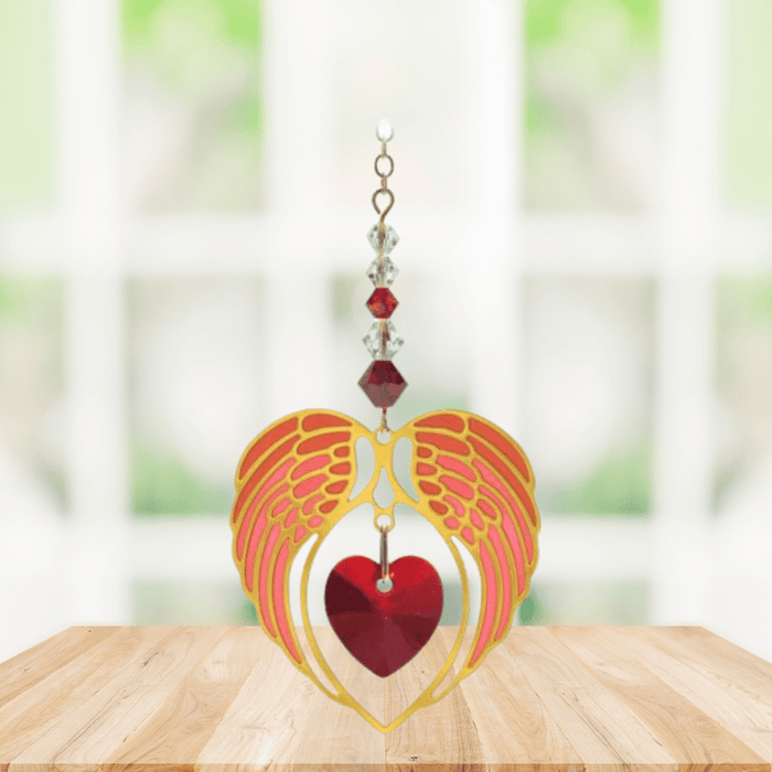 Gold angel wing heart suncatcher with garnet red crystal heart hanging in a bright window
